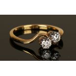 A gold and diamond two stone ring, claw set with circular cut diamonds in a cross-over design,