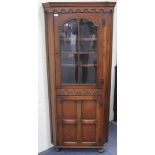 A 20th Century Jacobean style oak corner cupboard, the moulded pediment above glazed and panel