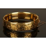 A 9ct gold hinged bangle with metal core, the front engraved with feathered scrolls, detailed '9ct