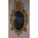 A 19th Century Rococo Revival giltwood and gesso oval wall mirror, the asymmetric pediment above