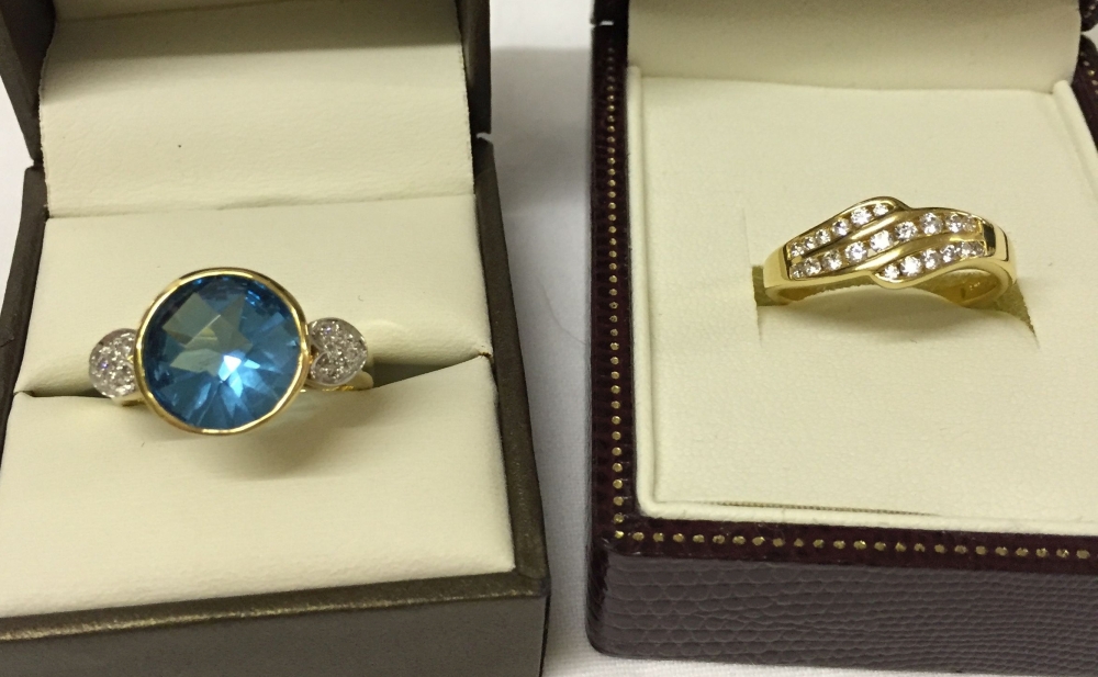 2 gold plated silver rings. One with large central blue stone size R, the other with 3 rows of white