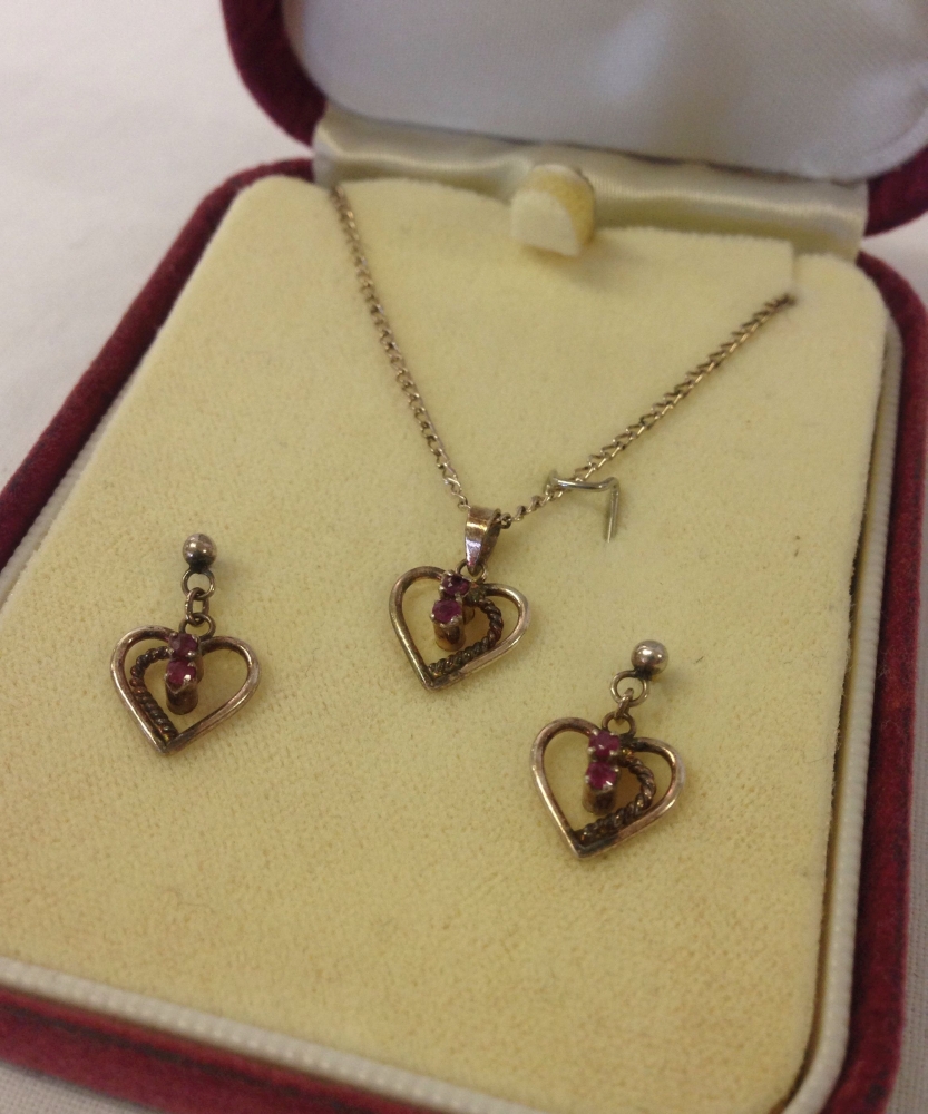 A boxed set of silver heart shaped earrings and pendant set with rubies. Pendant on an 18" silver