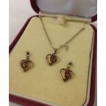 A boxed set of silver heart shaped earrings and pendant set with rubies. Pendant on an 18" silver