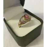 Gold dress ring set with a large oval pink topaz, set high on a mount with white and pink stones.