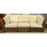 A cane 3 sectional conservatory sofa with plush cream cushions.