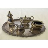 A silver plated condiment set on oval tray with spoons & blue glass liners.