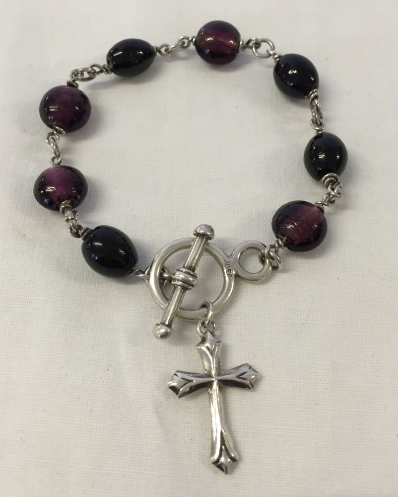 A silver bracelet with purple glass beads, a cross and T bar fastening.