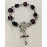 A silver bracelet with purple glass beads, a cross and T bar fastening.