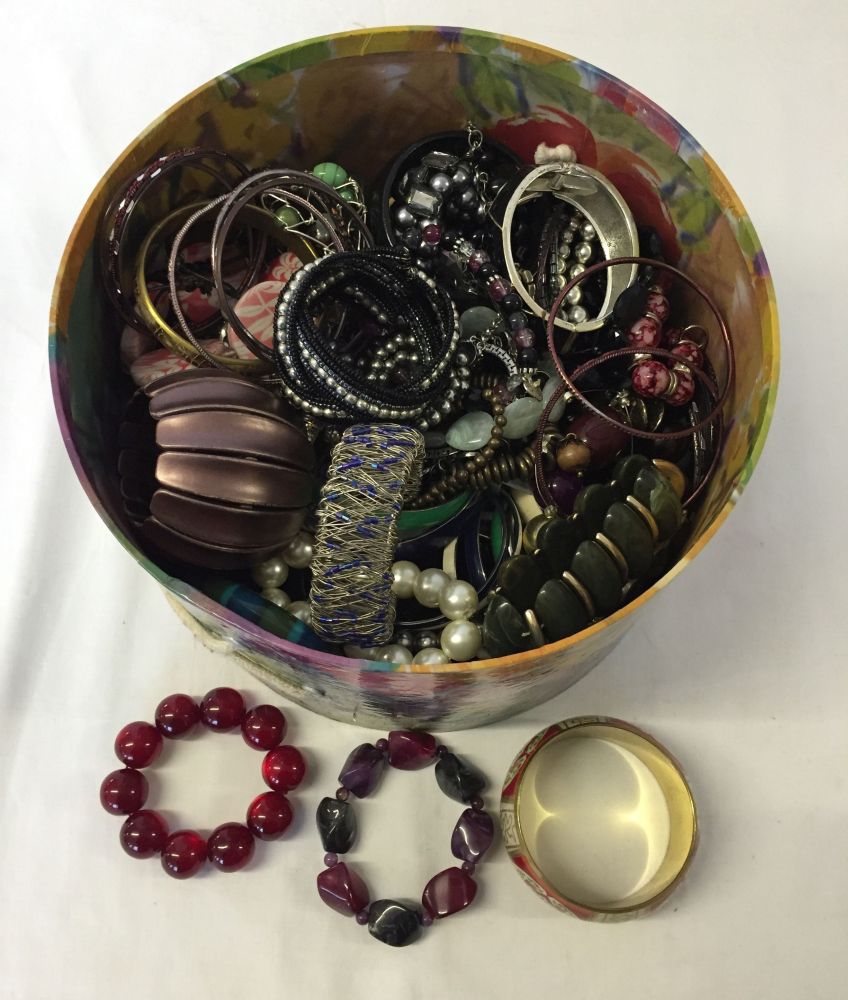 A round box containing a large quantity of costume jewellery bangles and bracelets.