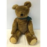 A vintage c.1920s straw filled teddy bear, approx 26 inches tall with plush fur and blue bow.