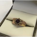 9ct gold dress ring set with central circular garnet surrounded by 8 clear stones. Size J½, approx