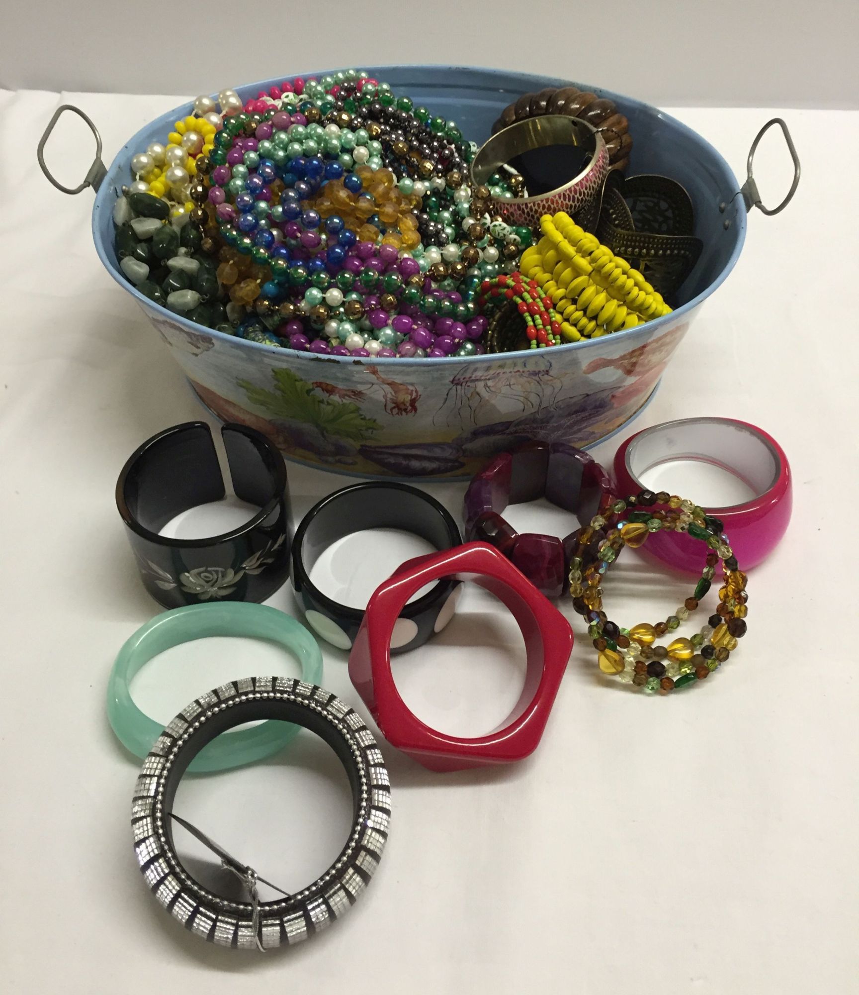 Tinplate tub containing a large quantity of costume necklaces and bangles.