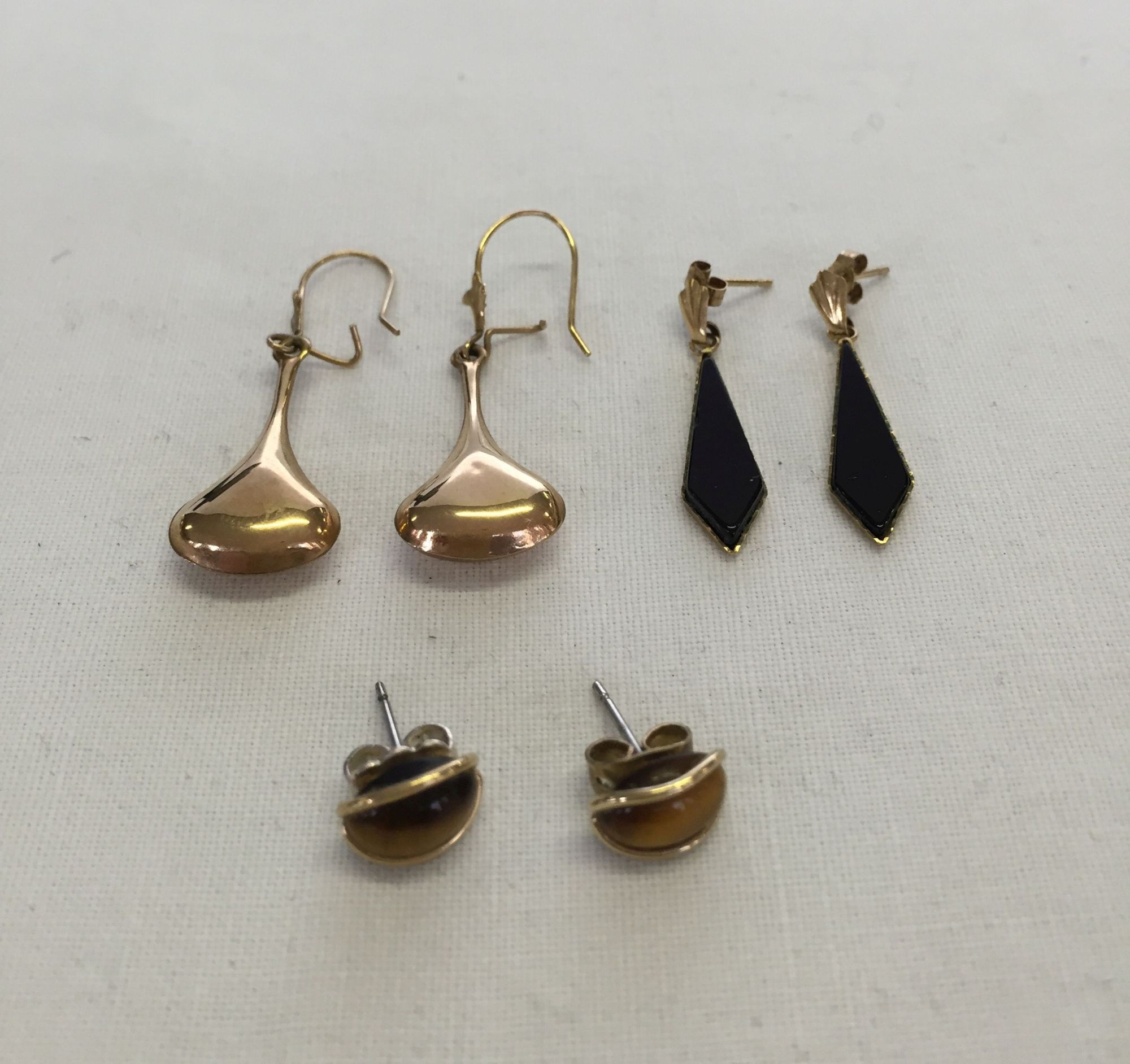 3 pairs of yellow metal earrings. One pair teardrop style, one pair drops set with onyx, and a