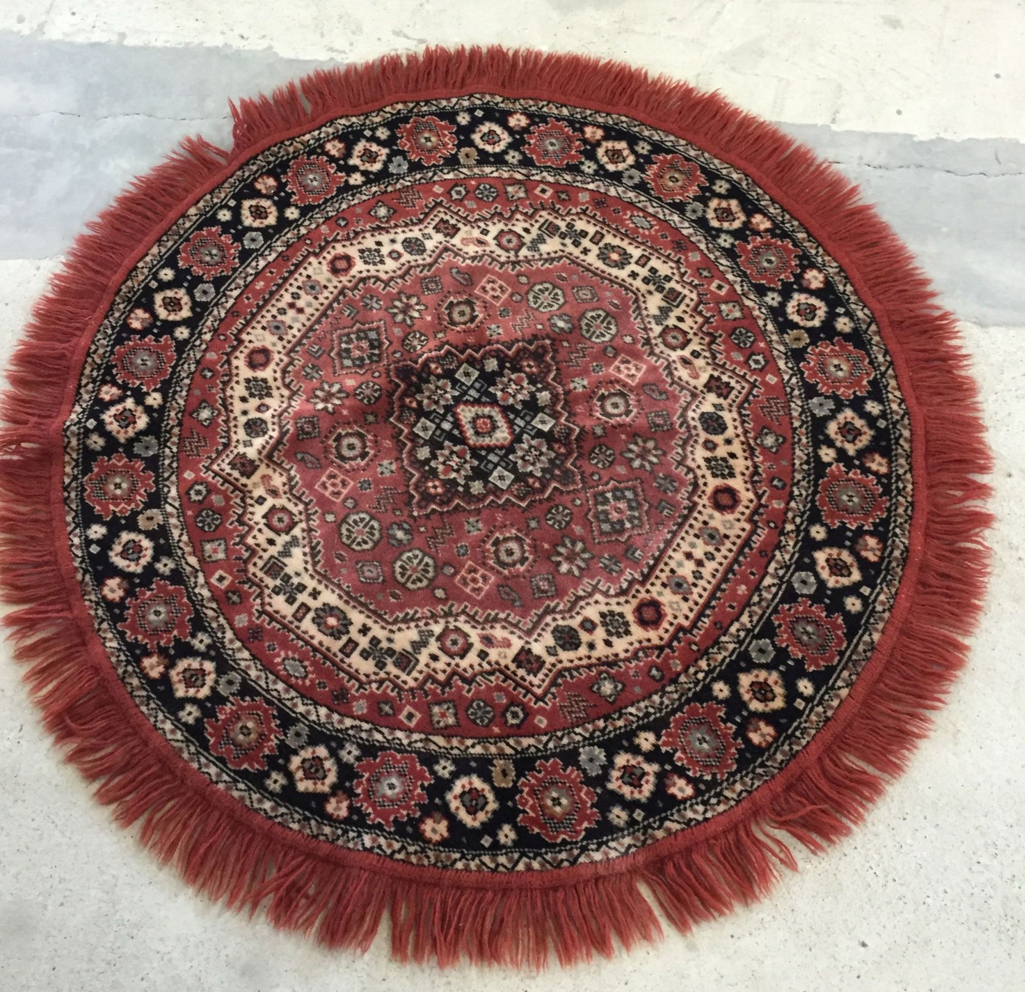 Red, cream and dark blue circular rug with fringing, approx 94cm in diameter.