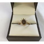 A 9ct gold dress ring set with a smoked quartz surrounded by small seed pearls. One pearl missing.