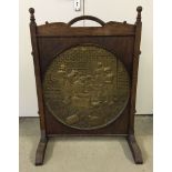 A large vintage wooden firescreen with central brass roundel depicting a tavern scene. Screen