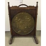 A large vintage wooden firescreen with central brass roundel depicting a tavern scene. Screen