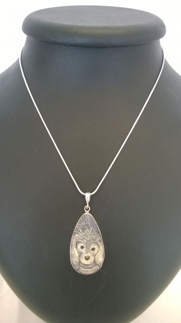 A dog face pendant carved in ox bone set in a 925 silver mount on a rope chain