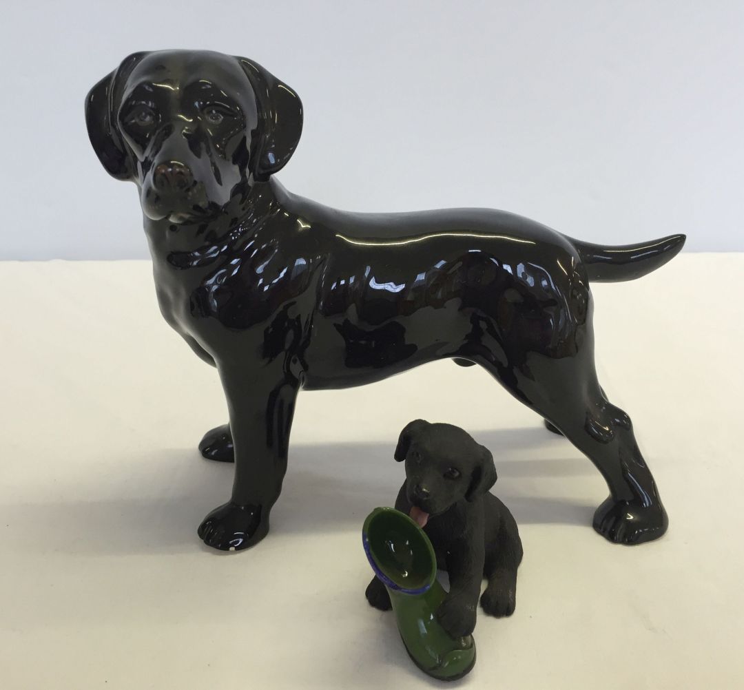 2 black Labrador figurines; 1) ceramic approx 19cm long 2) resin puppy with boot approx 9cm long.