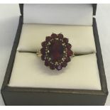 A 9ct gold garnet dress ring. A large central garnet surrounded by 14 smaller round garnets. Size