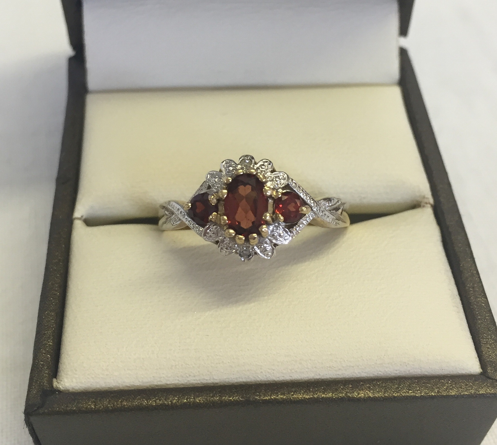 A 9ct gold dress ring set with garnets and diamonds. Central oval garnet with two smaller garnets