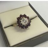 A 9ct gold garnet and diamond dress ring. A central diamond surrounded by 10 round garnets. Size