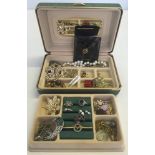 A small green and cream jewellery box containing a mixed selection of costume jewellery to include