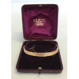 A 9ct gold opening bangle with safety chain. Engraved floral pattern on one side. Hallmarked Chester