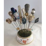 A collection of 20 vintage hat pins of different designs in a ceramic pin cushion holder.