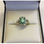 A boxed c1930s 18ct gold emerald and diamond ring. Baguette cut emerald surrounded by a circle of