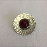 An arts and crafts style silver brooch set with a central carnelian stone.