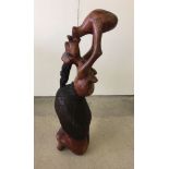 A tribal art wooden sculpture of a semi naked woman drinking, 80cm high.