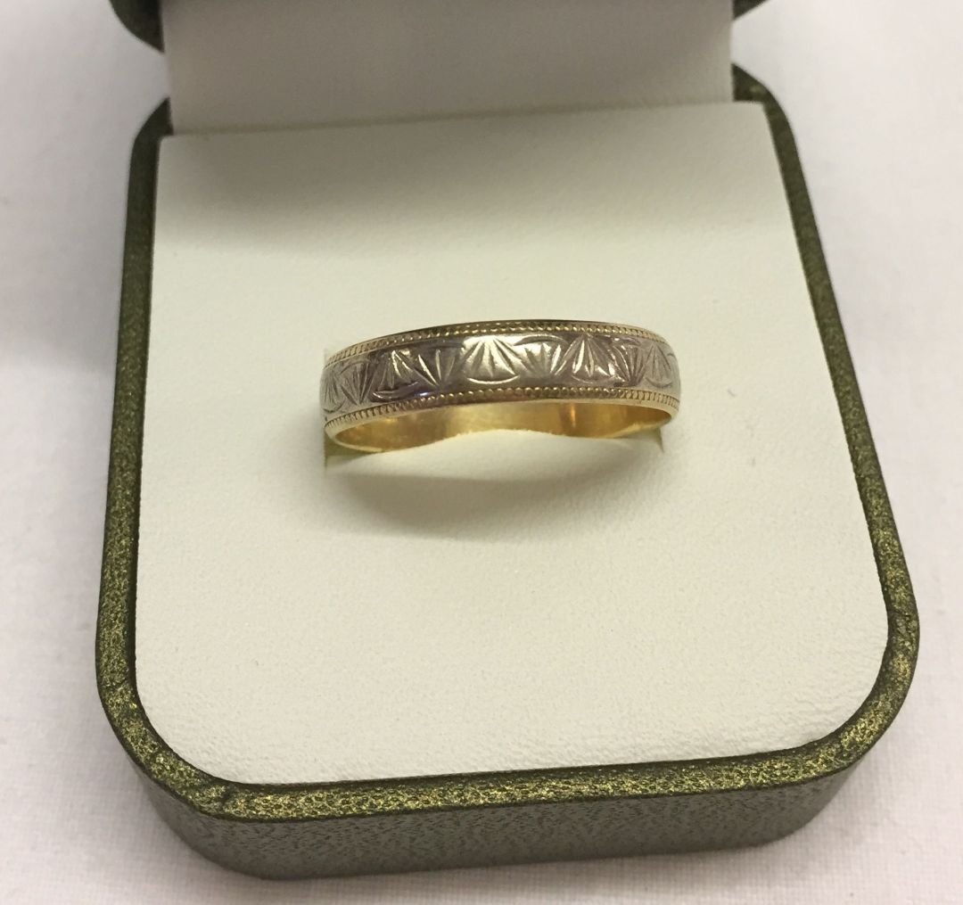 A 9ct two tone gold engraved pattern wedding band size V1/2. Total weight 2.7g.