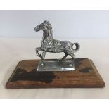 A silver plate figure of a horse on a small wooden plinth, possibly car mascot.