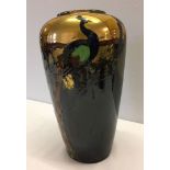 A ceramic vase of brown/green colouration with a Peacock sitting in front of golden sunshine. Approx