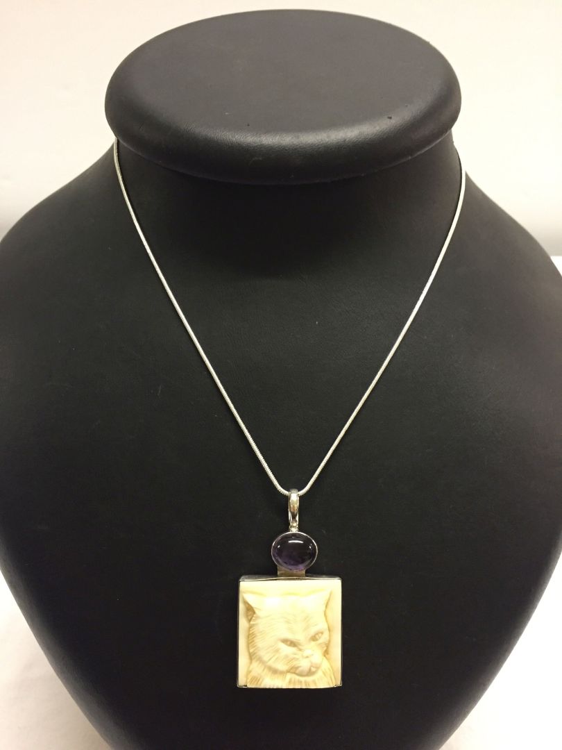 A carved cat face pendant set with an amethyst cabouchon with 925 silver bale and setting on a