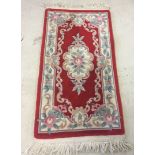 A small rectangular red and floral rug. Approx 148cm x 70cm