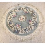 A small circular rug, pale blue with floral design. Approx diameter 116cm with fringe