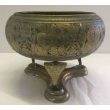 A large brass bowl with oriental carved detail sitting on a snake head stand.