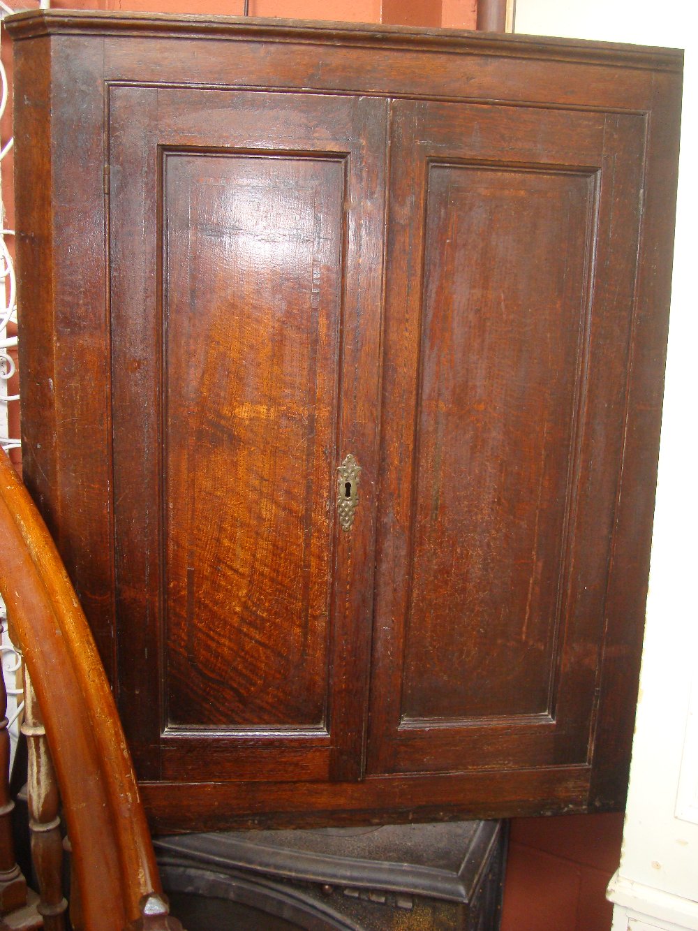 A George III oak hanging corner cupboard, with panelled doors enclosing shelves with shaped edges.