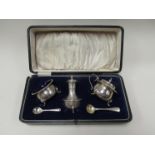 A three piece silver cruet set in fitted box with silver spoon and one plated spoon,