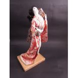 A late 20th Century Geisha girl figure in traditional clothing on wooden base,