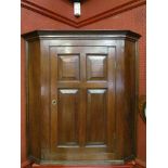 A Georgian elm corner hanging cupboard with four panelled door and a shaped shelved interior