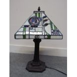 A Tiffany style table lamp with stylised flower and cabouchon stone inlaid on a flared bronzed