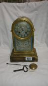 A brass arched top 8 day clock with ceramic dial, ceramic front plaque, key and pendulum