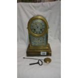 A brass arched top 8 day clock with ceramic dial, ceramic front plaque, key and pendulum
