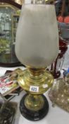 A brass oil lamp on black pottery base and with frosted glass shade