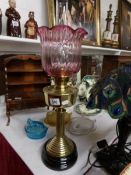 A brass oil lamp on black pottery base and with later cranberry glass shade