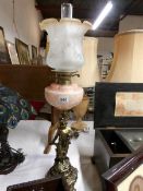 A gilded spelter cherub oil lamp with mottled amber glass font and amber tipped acid etched shade