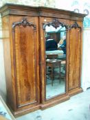 A Victorian mahogany triple door wardrobe having 2 flame mahogany on one mirrored door